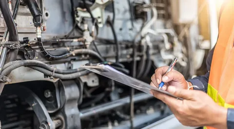 A Foersch Contracting technician in a high-visibility vest completing a maintenance checklist while inspecting complex industrial machinery.